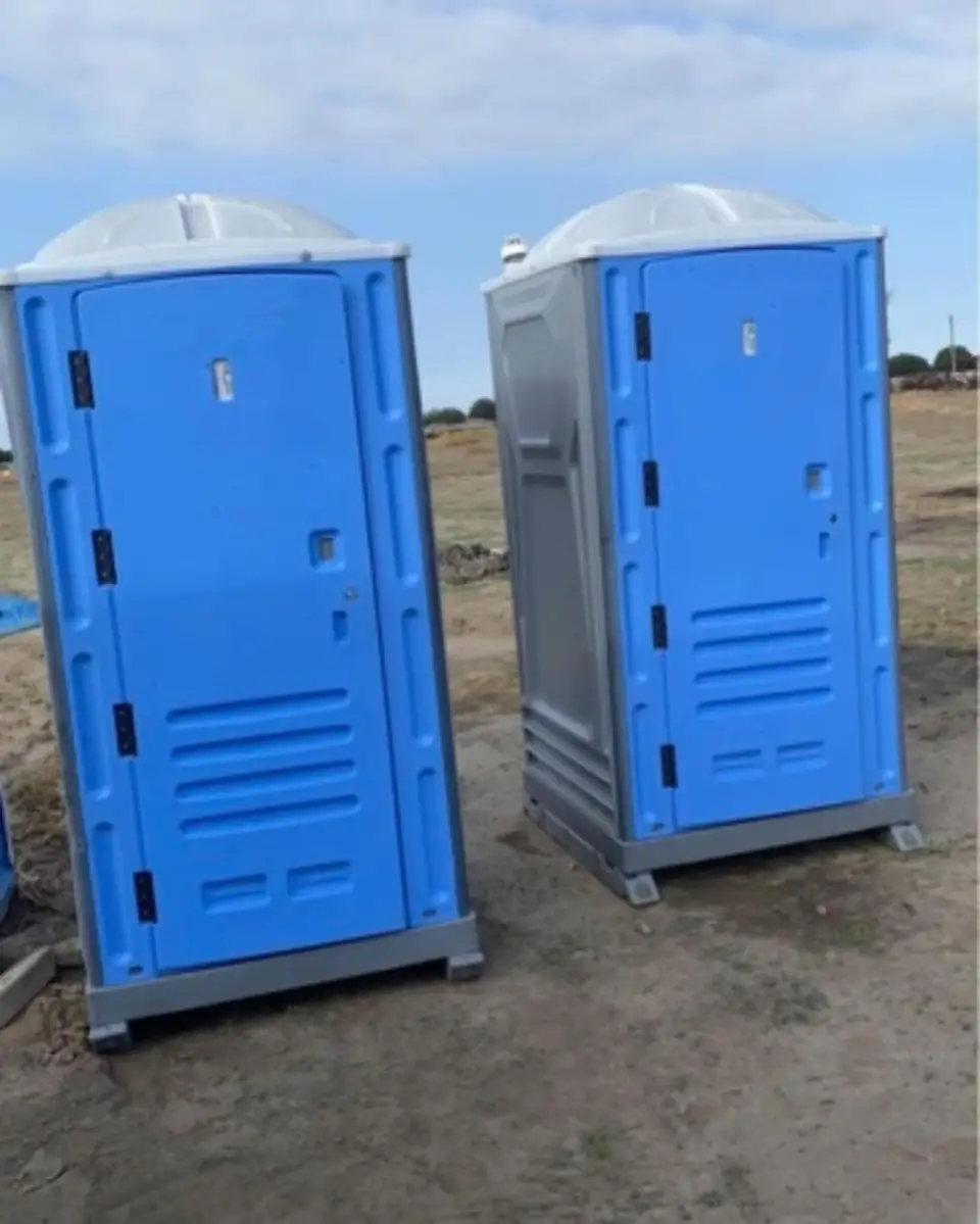 Two blue porta potties set on bare dirt at a construction site