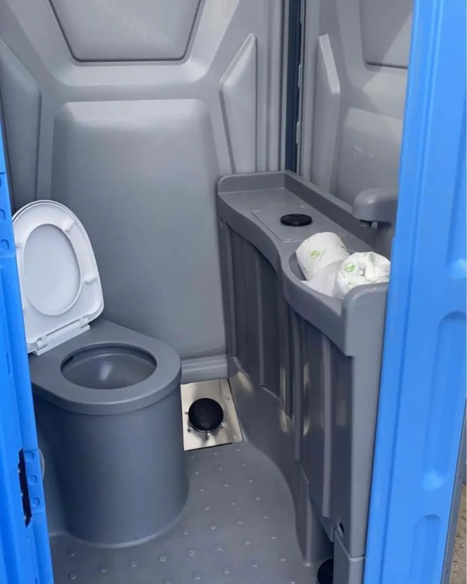Inside a deluxe porta potty with a toilet seat and a built-in sink basin