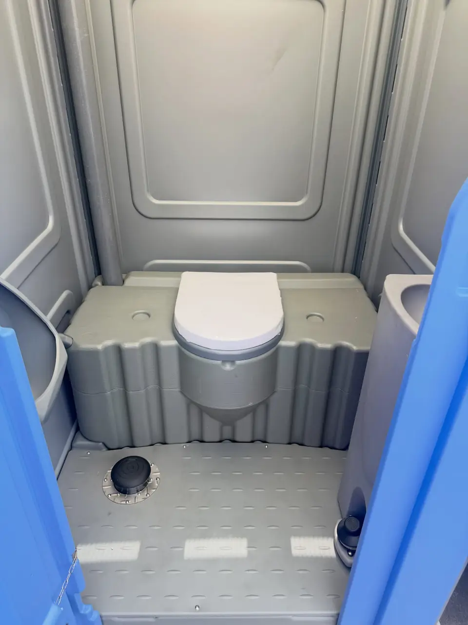 Interior of a flushing porta potty with a white toilet seat