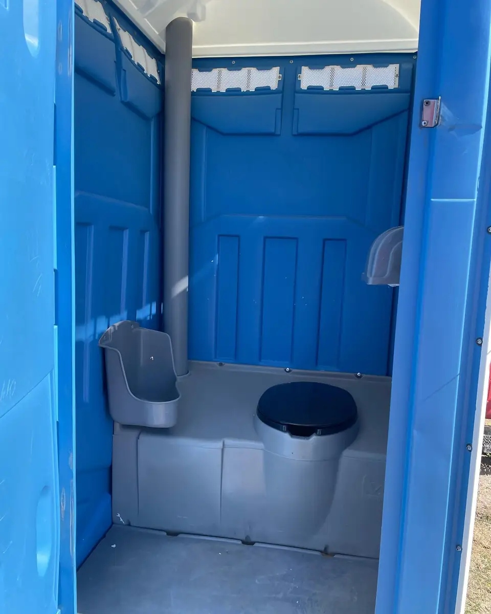 Wide interior view of a blue standard porta potty with seat and urinal