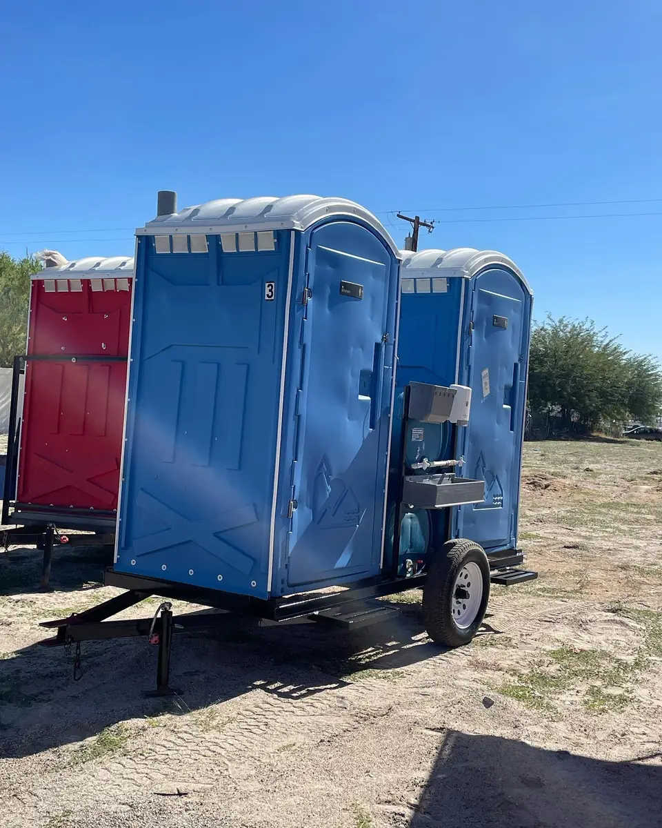 Blue porta potty mounted on a small towable trailer at a jobsite