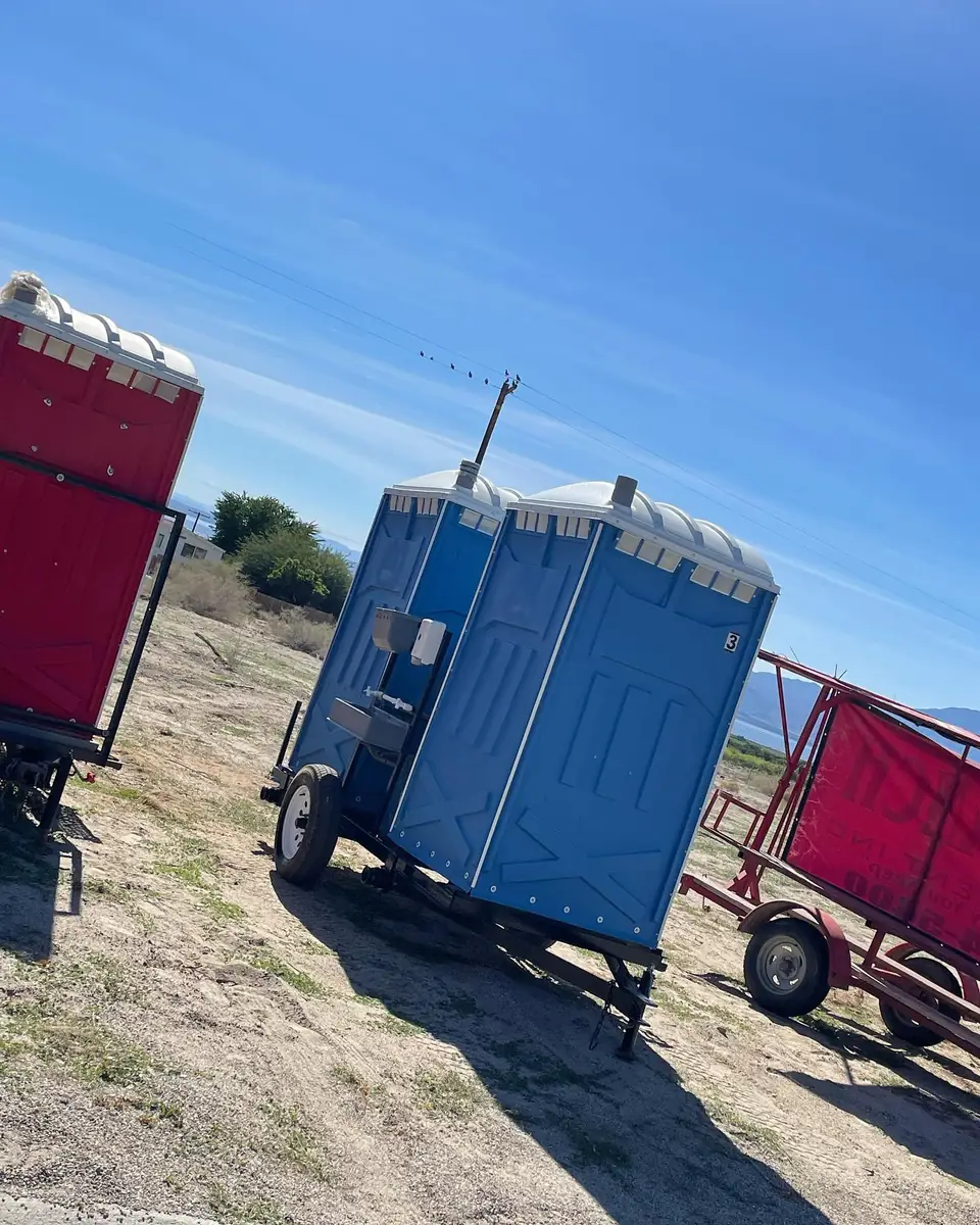 Towable porta potty trailer parked on a dirt lot next to a work trailer